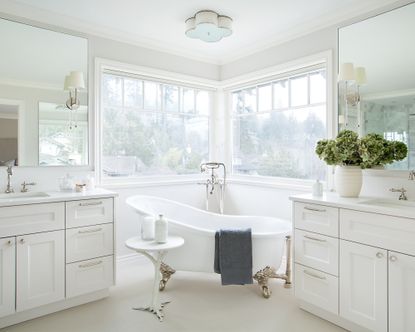 A white bathroom with a freestanding tub in front of a double corner window 