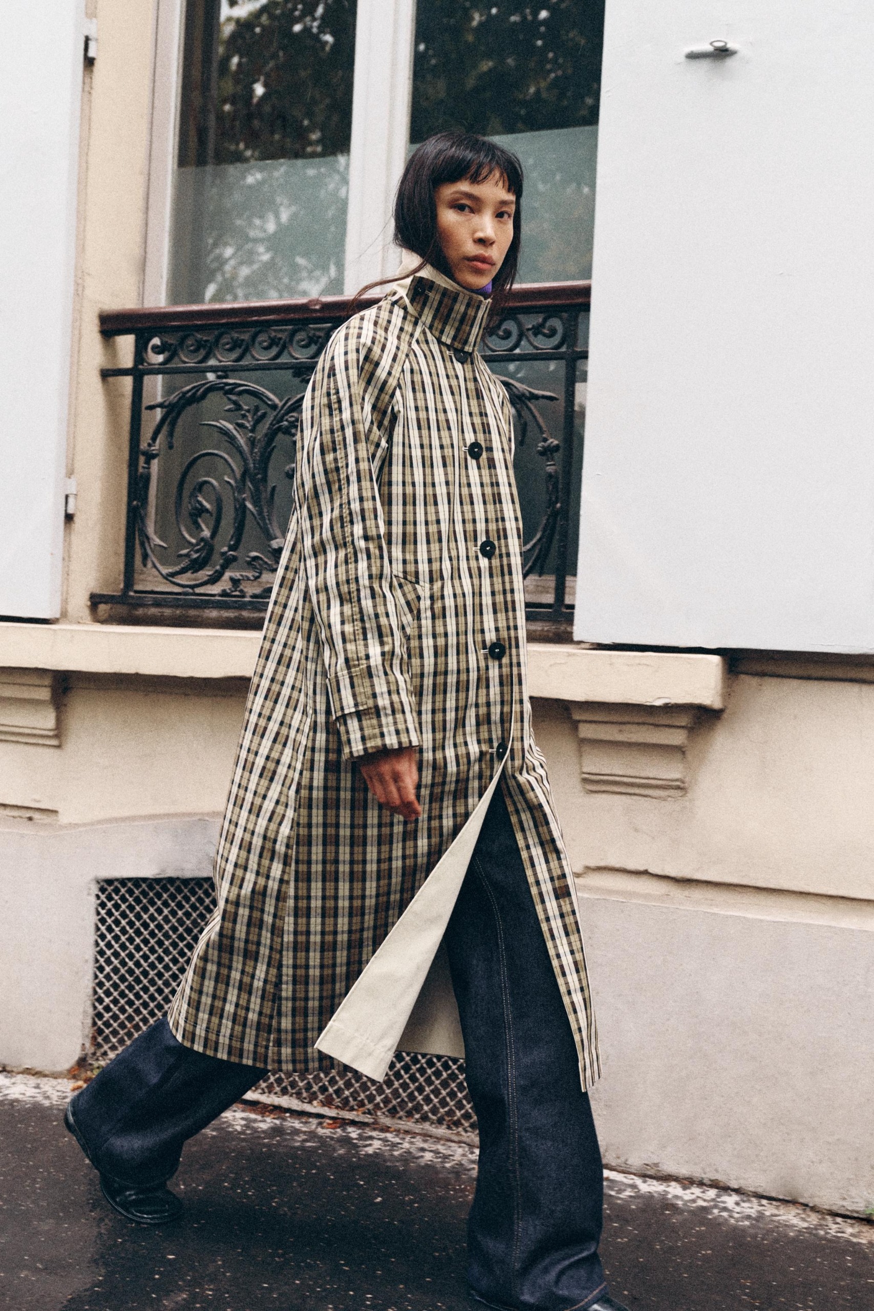 A Zara model wearing a long, checked coat and dark wash jeans