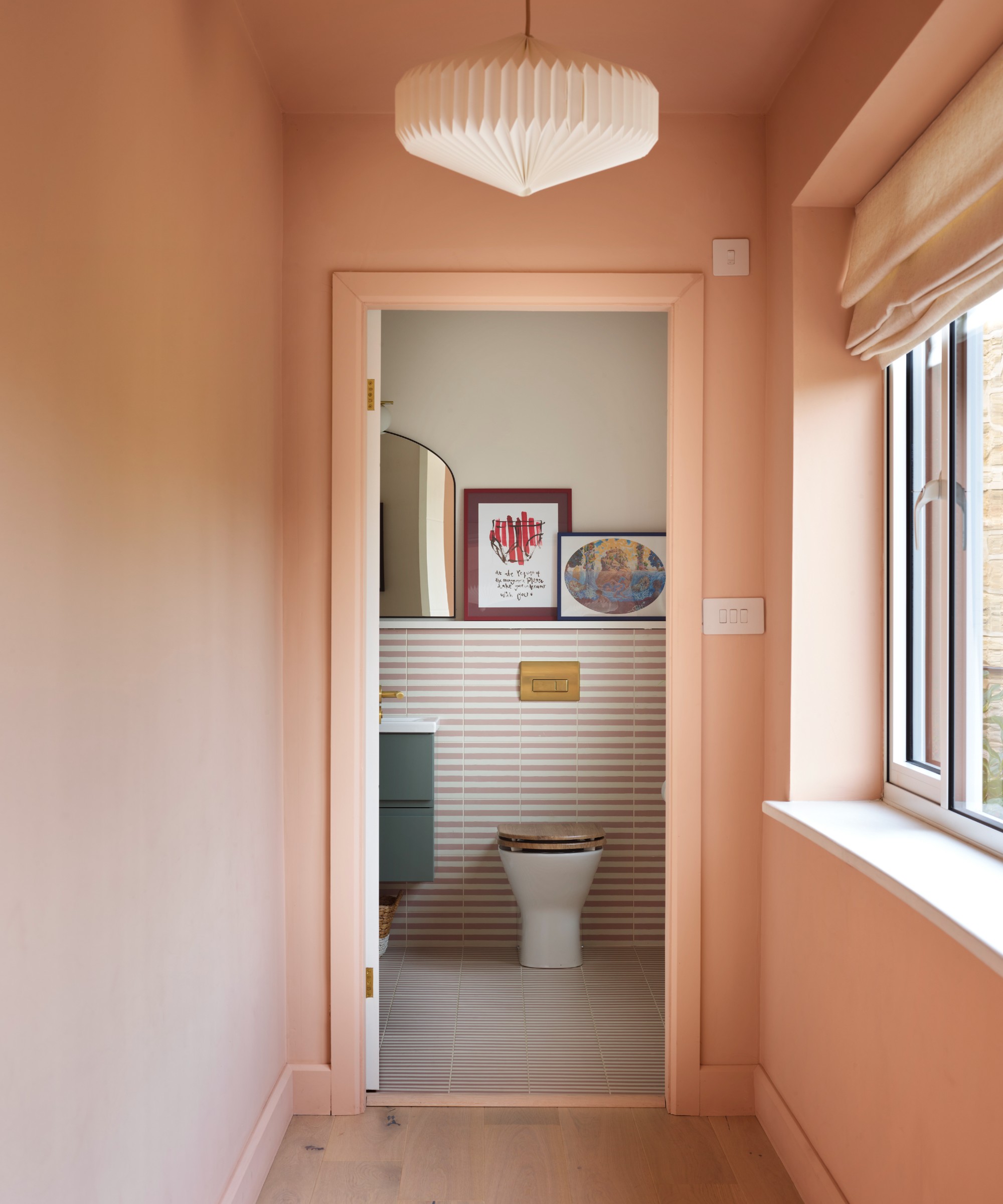 A hallway colour-drenched in a light pink shade with a paper lantern-style pendant light