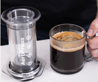 Aeropress next to a cup of coffee