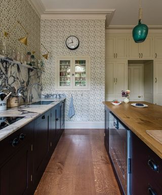 a london kitchen designed with floral wallpaper with dark cabinetry and warm wood floor with a mix of marble and wooden countertops