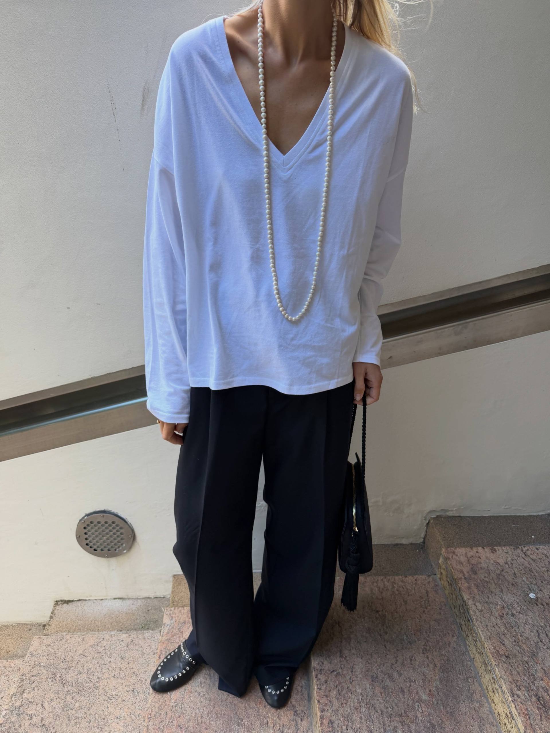 Linda wears a white v-neck, black trousers, and black loafers.