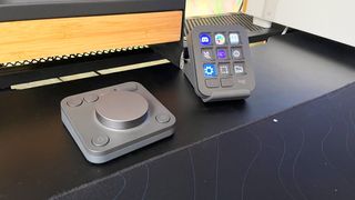 The Logitech MX Creative Console on a black desk in front of a wood monitor stand