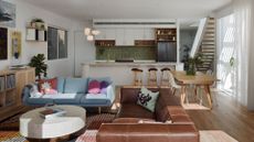 A colorful living room with pendant lights, a brown leather sofa, a blue couch, a round coffee table and houseplants in an open concept living room and kitchen space