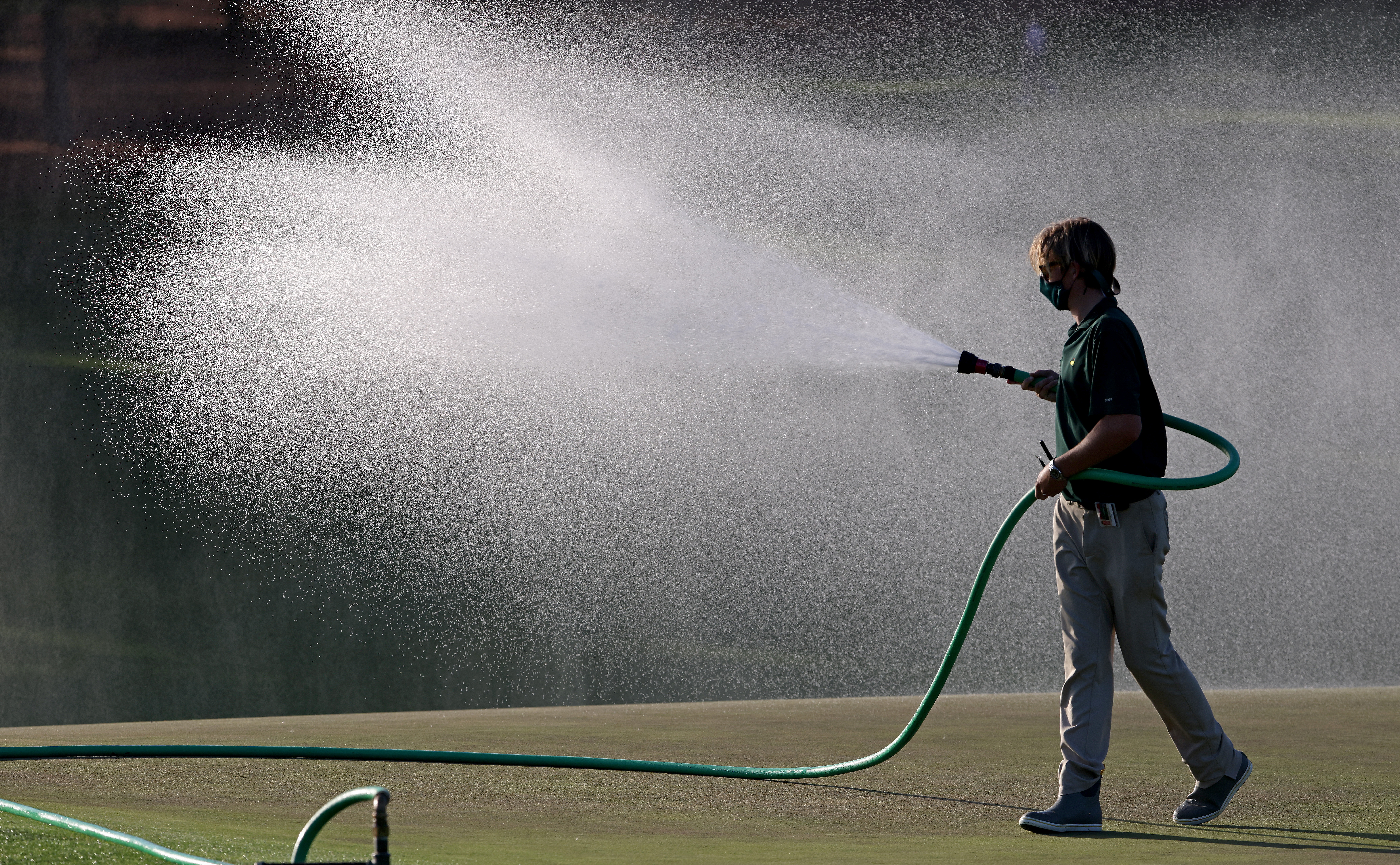 A member of the grounds crew waters the course during a practice round prior to the Masters at Augusta National Golf Club