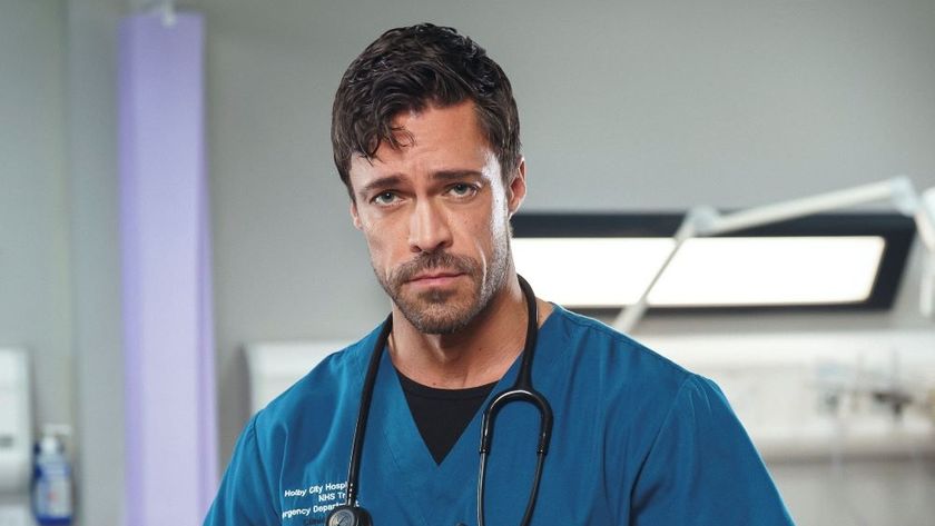 Olly as Casualty&#039;s new Clinical Lead Flynn Byron wearing blue scrubs and standing in a hospital, looking into the camera with a serious look on his face