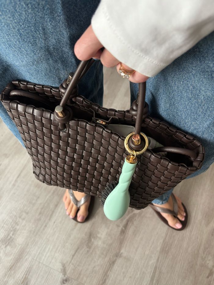 A brown handbag with a mint green La Bonne Brosse hairbrush bag charm attached