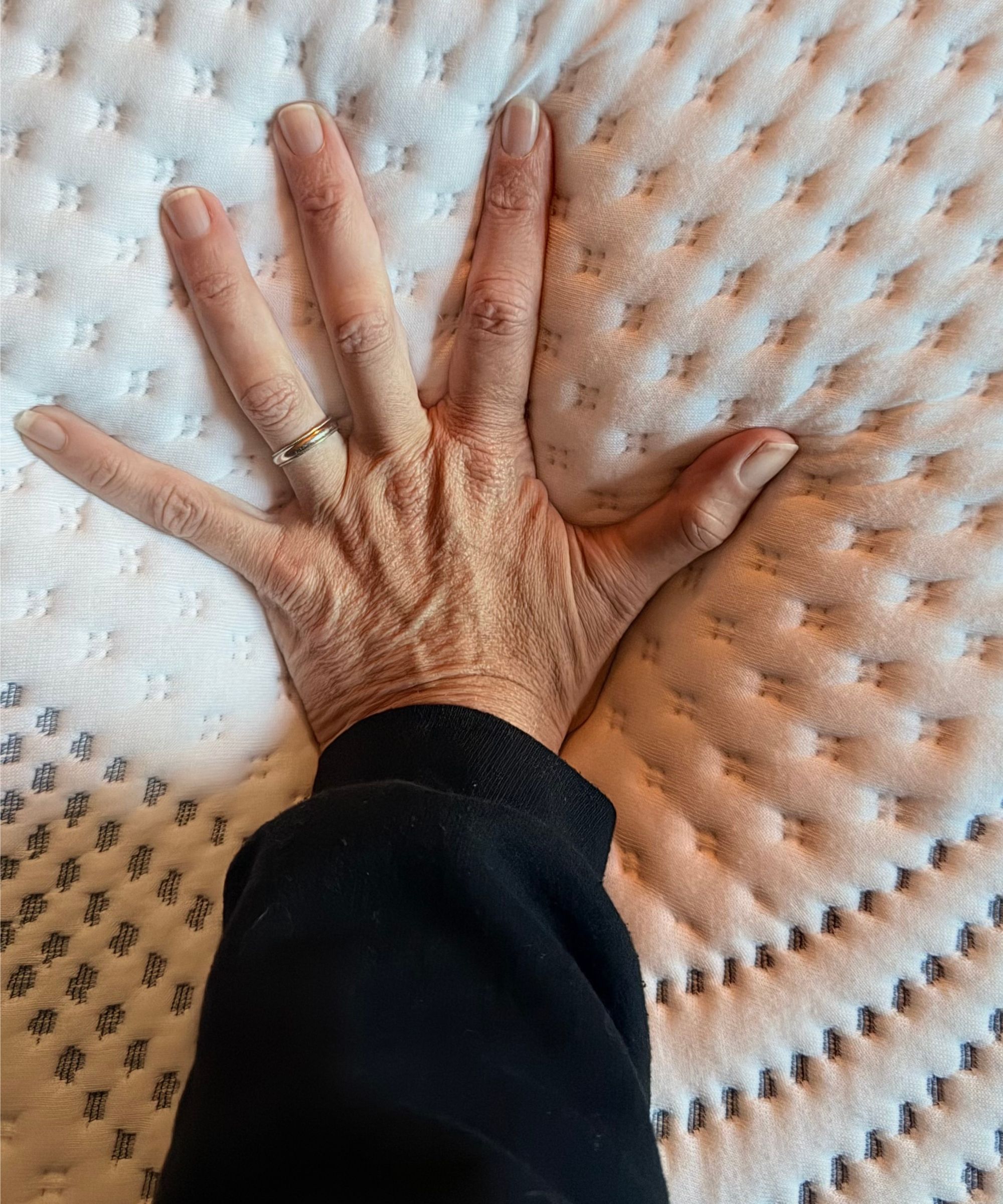 A woman's hand pressing into a white mattress surface.
