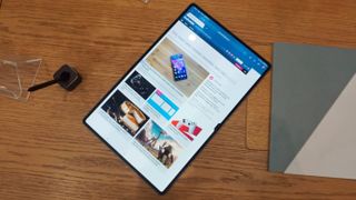 En Samsung Galaxy Tab S8 Ultra ligger uppåtvänd på ett träbord bredvid en stylus och en laptop, med TechRadar-hemsidan uppe på skärmen.