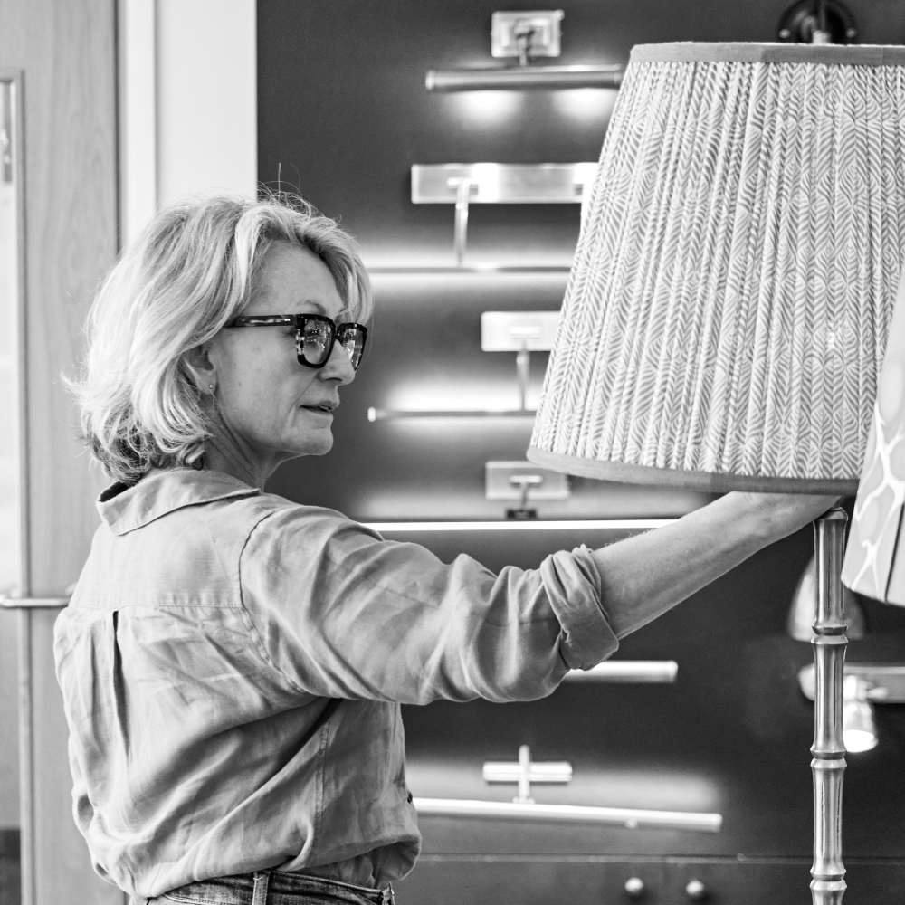 female with short bob, glasses wearing shirt adjusting the shade of a floor lamp