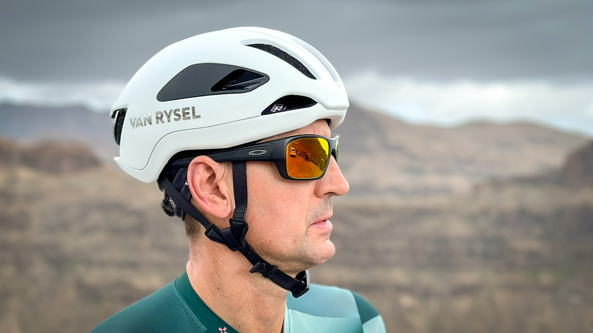 side view of a man wearing a white helmet, black sunglasses and a green jersey