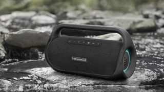 Tronsmart Bang Mini Bluetooth speaker on a water bank outdoors in the daytime.