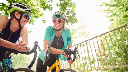 Two women taking a rest while riding bikes, aerobic exercise for brain health, wearing helmets and cycling activewear, smiling in the sunshine