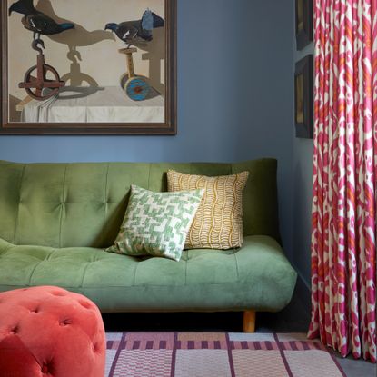 A blue-painted living room with a green sofa bed with a patterned rug and an artwork hanging on the wall