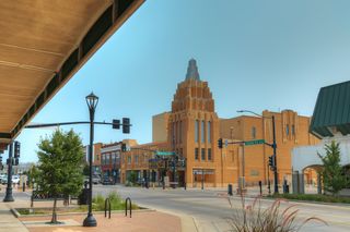 A street scene showcases an ornate brick building with a stepped design, characteristic of Art Deco architecture. The area is calm, with a clear sky and some greenery along the sidewalk. Santa Fe Avenue Salina, Kansas Photo taken on July 25, 202