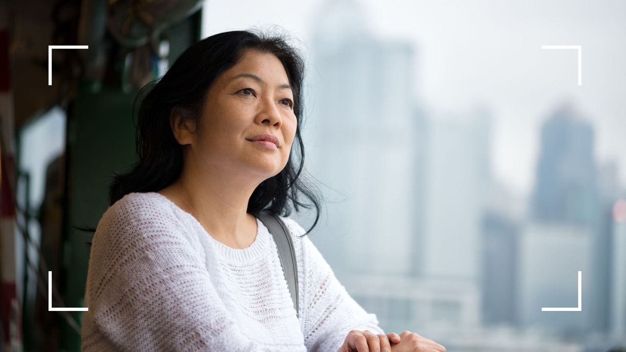 Woman looking of the window in city high rise office at work, wondering can menopause affect your confidence