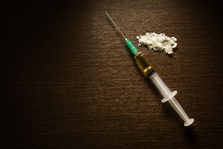 A syringe next to powdered heroin.
