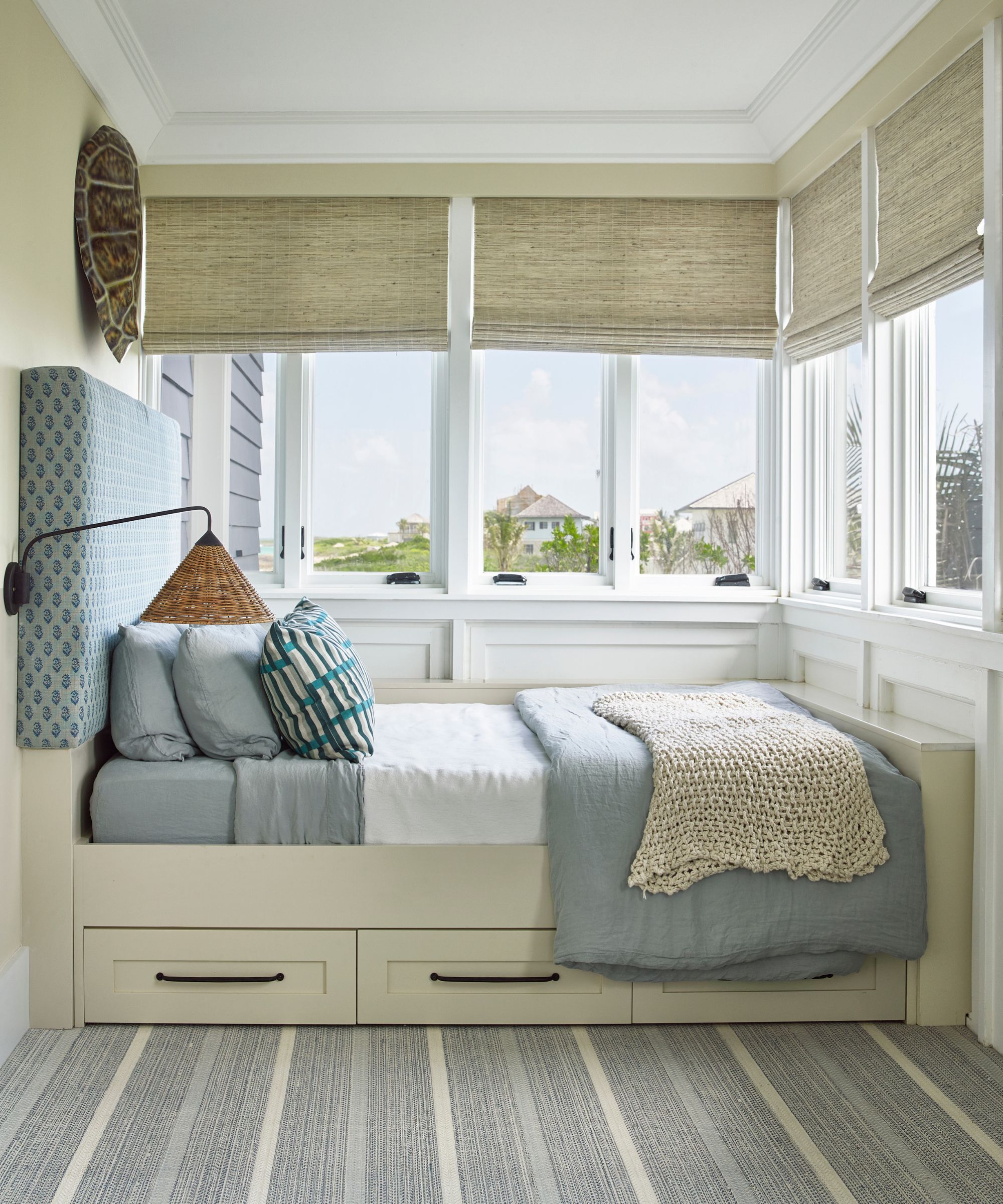 Sleeping porch with rattan blinds, striped carpet, built-in bed with blue and white bedding and rattan sconce