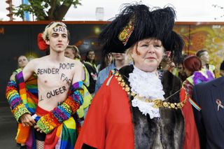 Half naked man walking behind a ceremonial mayor at a Pride march
