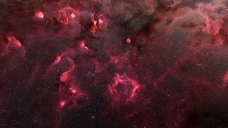 Reddish-pink nebulas spread their tendrils across a backdrop of sparkling white stars.
