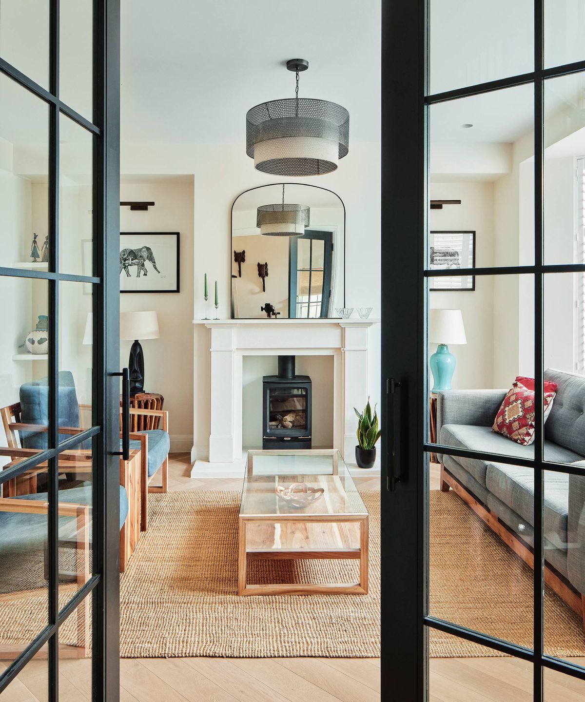 Living room with black Crittal-style doors and rattan rug, glass coffee table with navy chairs and grey sofa