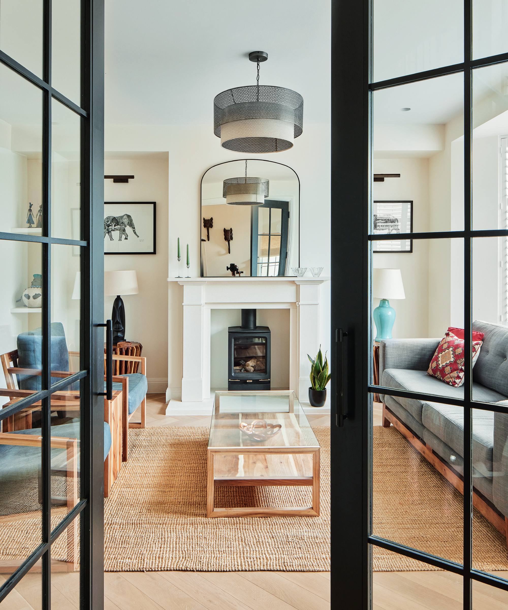 Living room with black Crittal-style doors and rattan rug, glass coffee table with navy chairs and grey sofa 