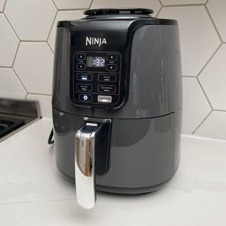 Side view of a Ninja AF100UK Air Fryer on a white worktop with white hexagonal wall tiles