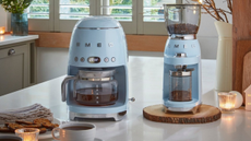 Smeg drip coffee maker in pastel blue with the matching grinder on a countertop