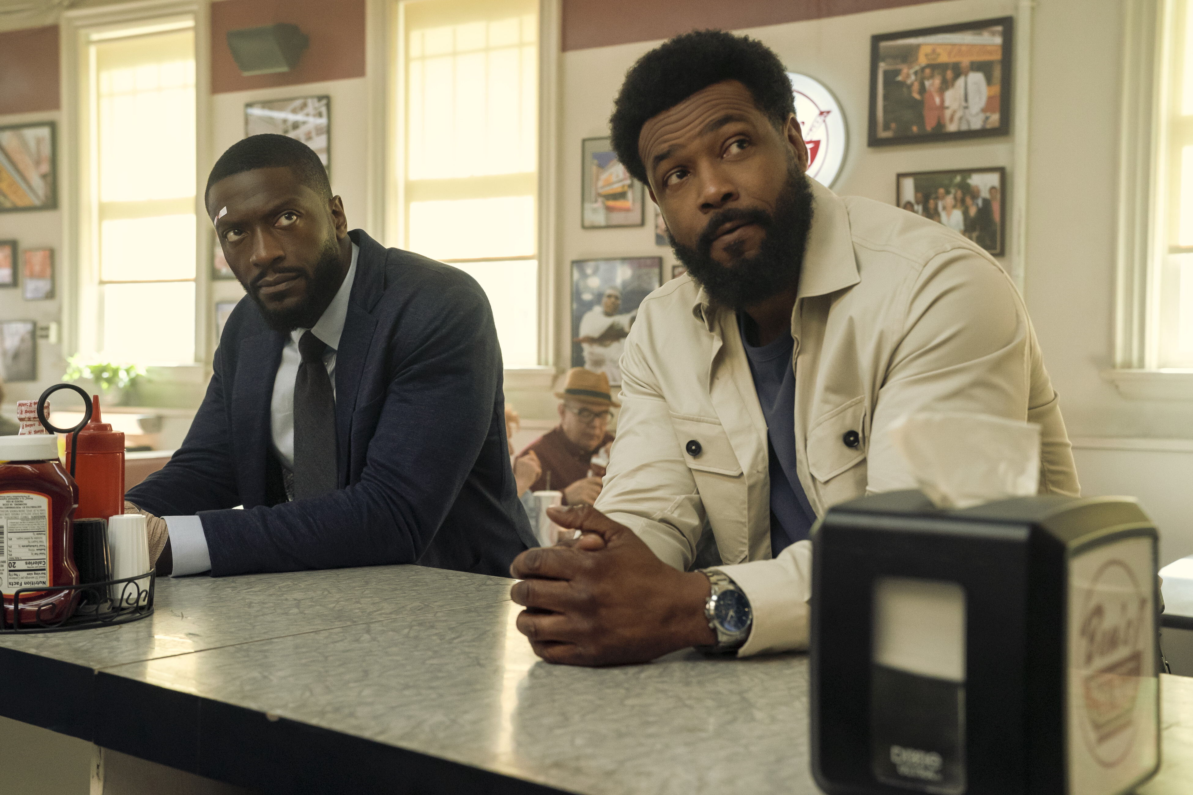 A still from 'Cross' season 2 of aldis hodge as alex cross and isaiah mustafah as john sampson sitting at a diner counter