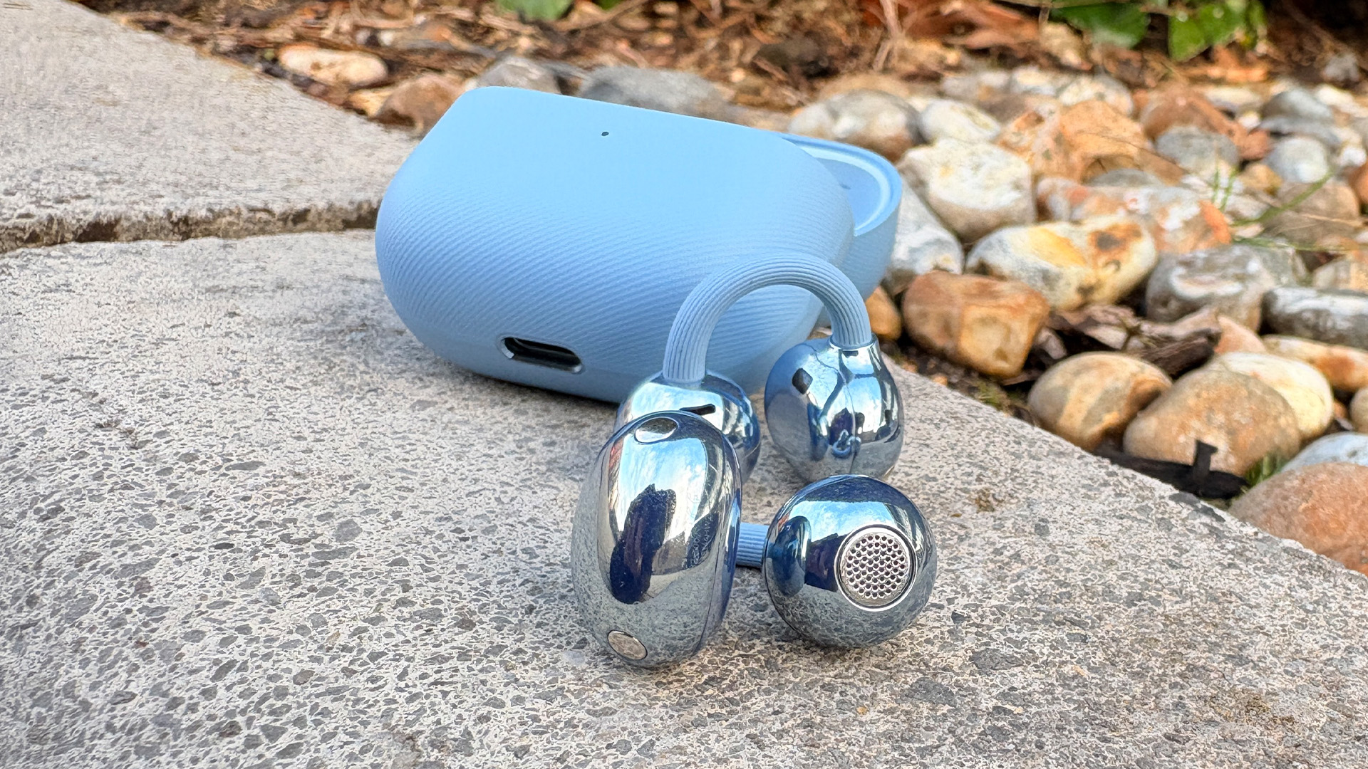 Huawei FreeClip 2 wireless earbuds on concrete next to open charging case