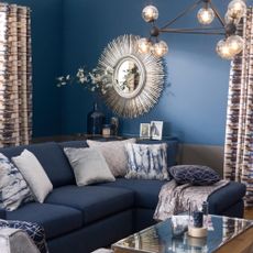 Dark blue living room,matching sofa, grey armchair, wood floorboards, modern lantern chandelier, glass coffee table, modern sunburst mirror.