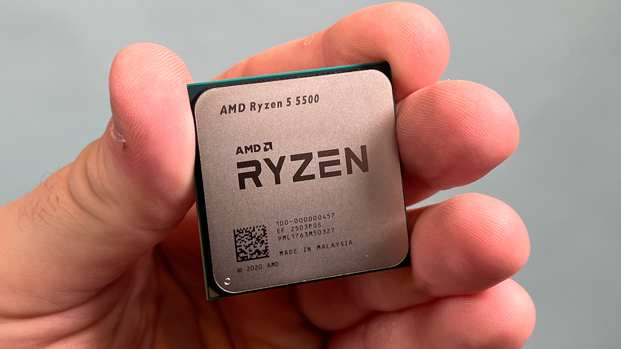 An AMD Ryzen 5 5500 held in a masculine hand