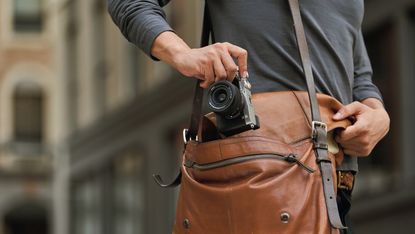 A man putting one of the best mirrorless camera, the Sony A7C, in his shoulder bag