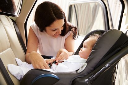A woman puts a baby in a carseat.