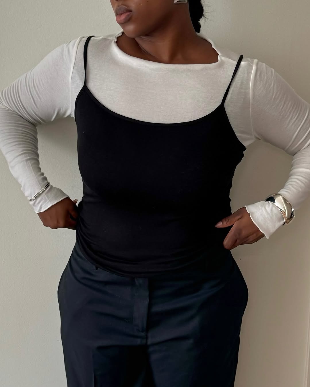 Influencer Nnenna wears a white long sleeve under a black tank and a black trousers.