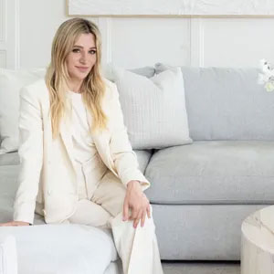 White woman with long blonde hair in cream suit sat on large couch is Victoria Holly