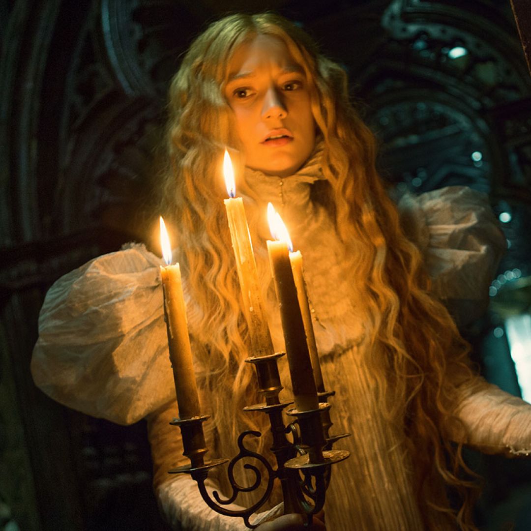 a woman in a white gown holds a candleabra walking through a spooky house in crimson peak