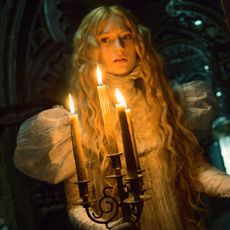 a woman in a white gown holds a candleabra walking through a spooky house in crimson peak