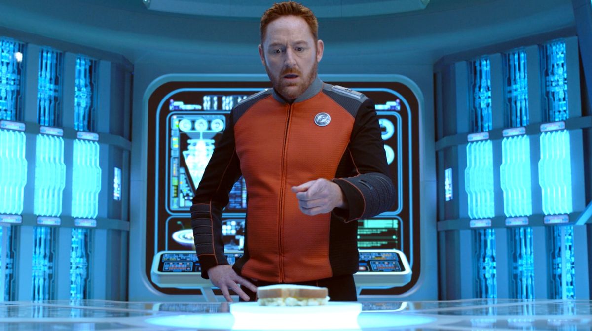 an actor in a futuristic uniform stands on the deck of a starship on the set of a sci-fi show