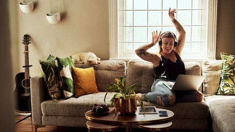Woman sits on couch listening to music with her arms in the air