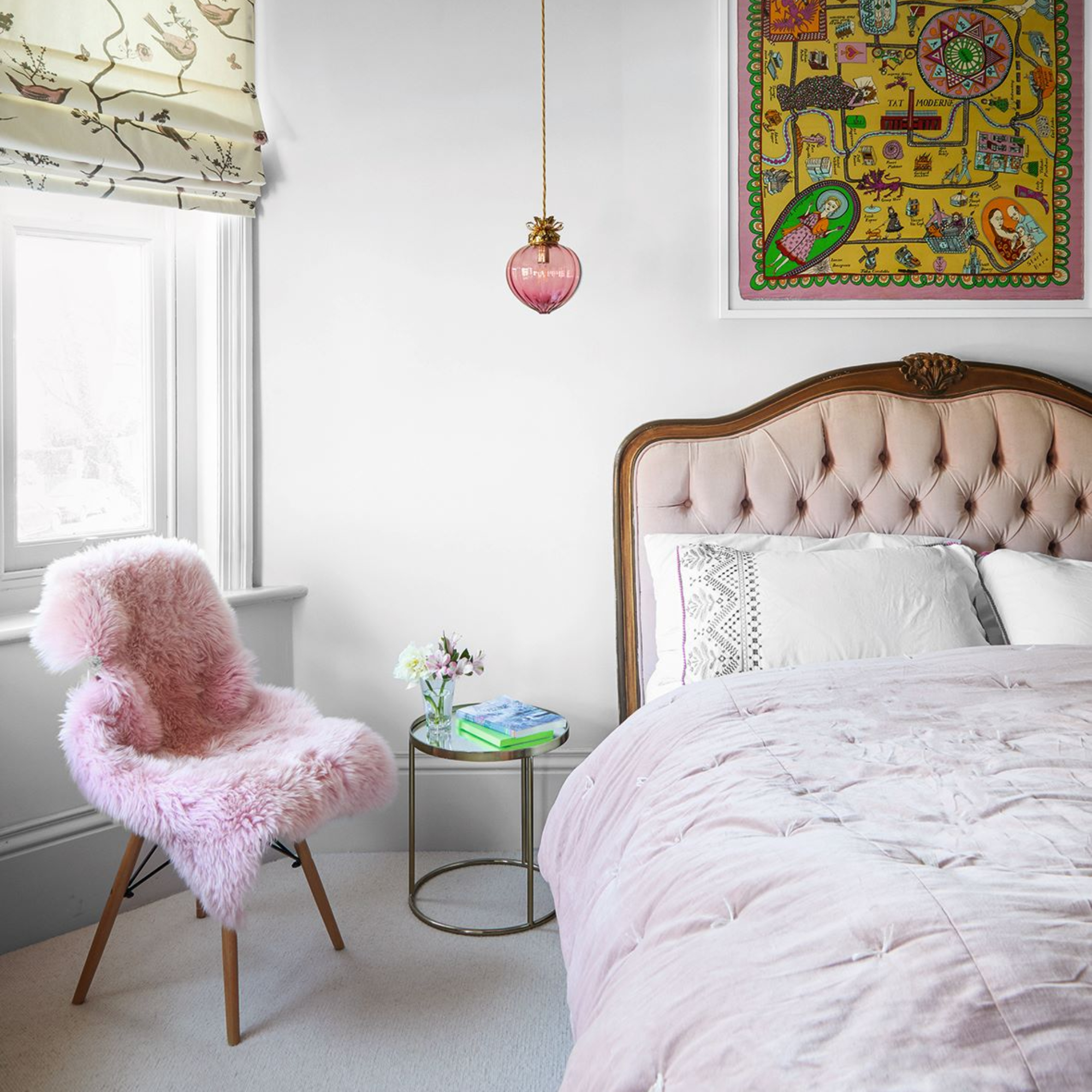 Padded bedstead and animal fleece in pale pink draped over chair in bedroom with bird pattern Roman blind and accent colour yellow tapestry on wall