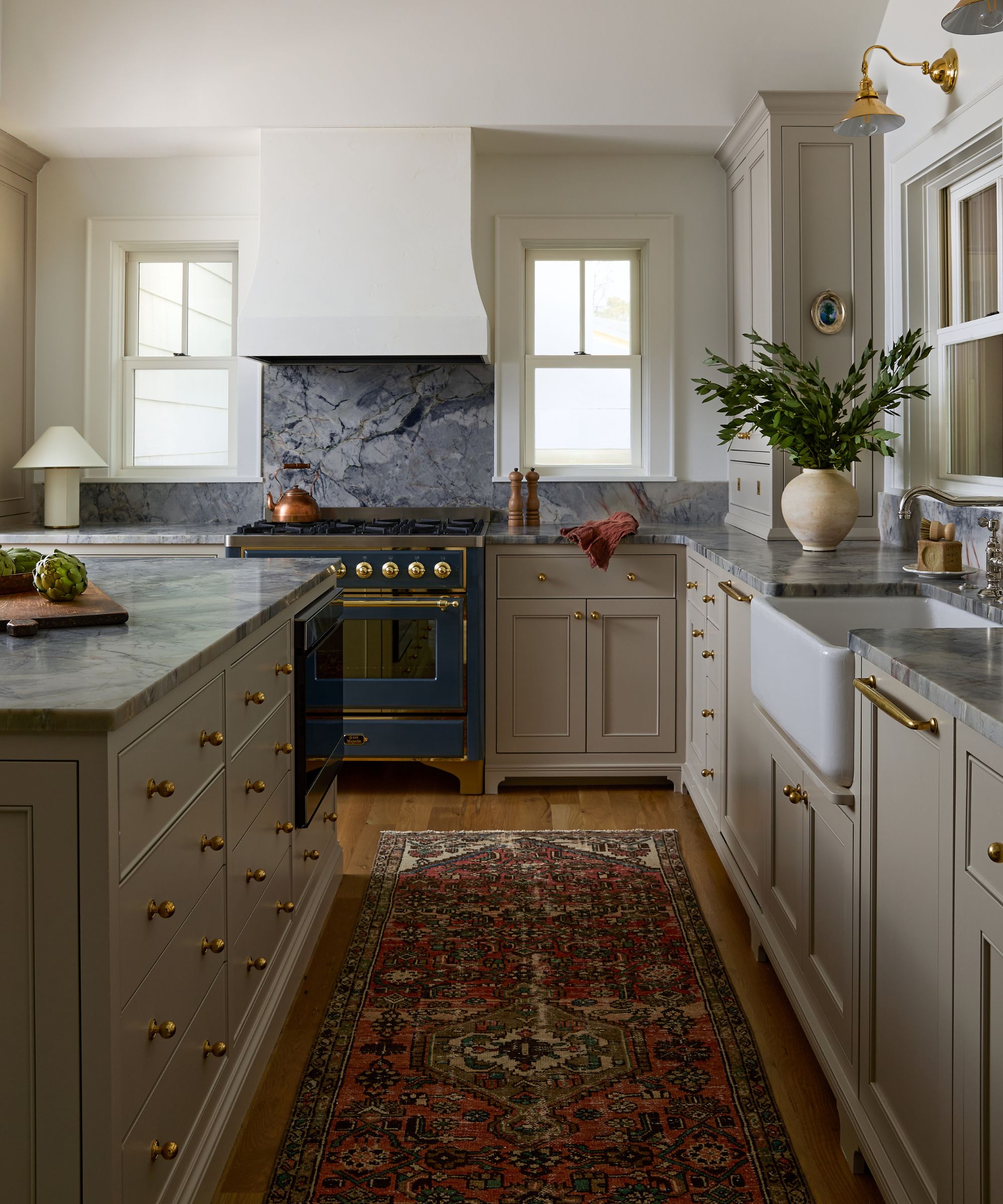earthy neutral kitchen with large windows out to the lakeside view, a large plaster cooker hood, and blue marble countertops