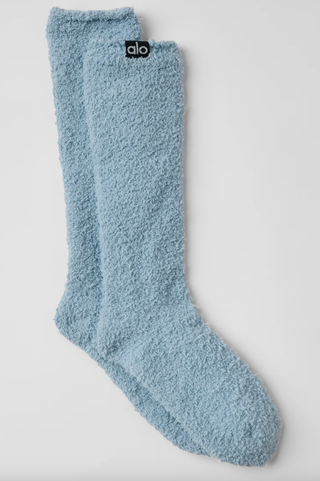 a pair of blue alo yoga fuzzy socks in front of a plain backdrop