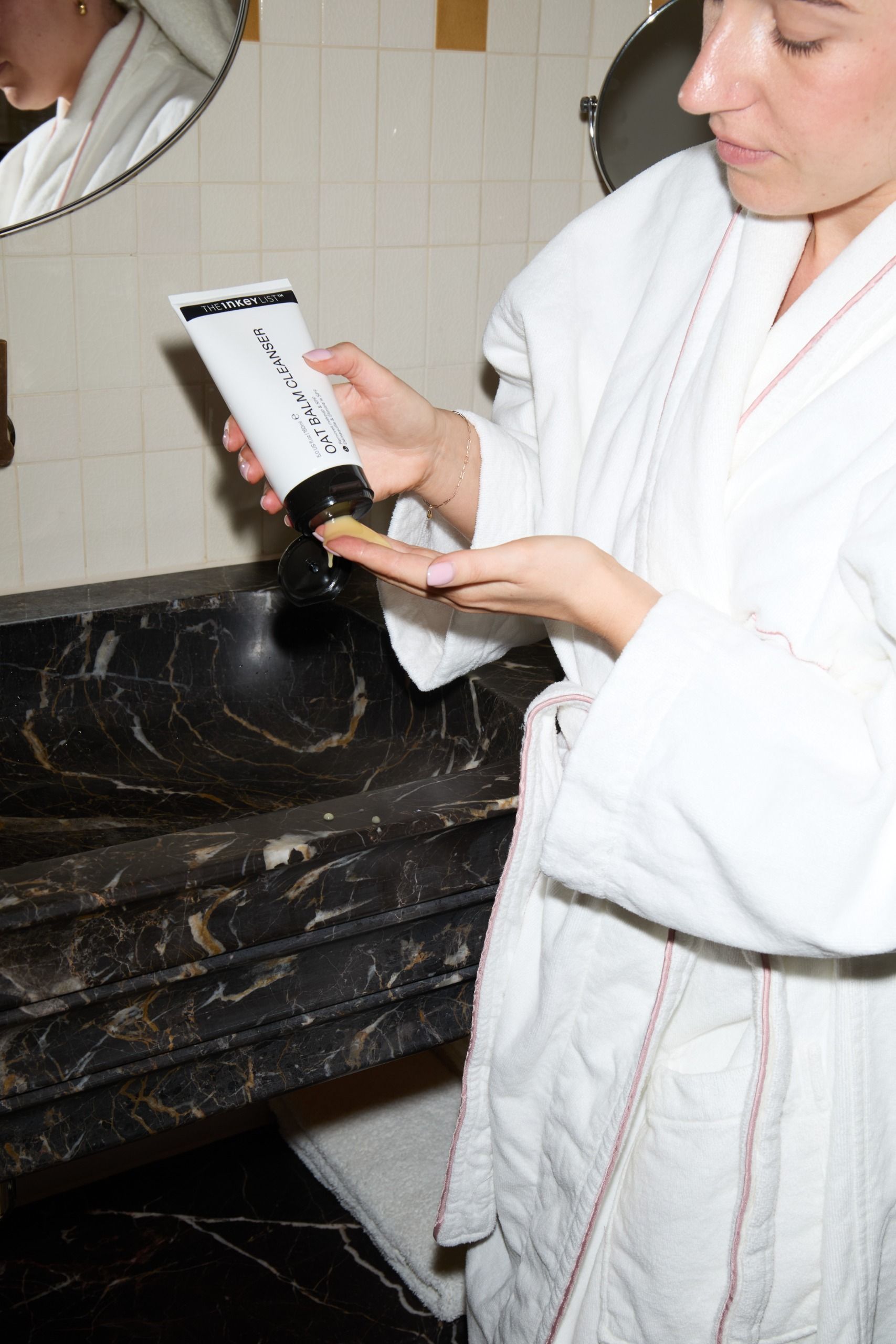 Grace Lindsay applying The Inkey List Oat Balm Cleanser next to a marble sink