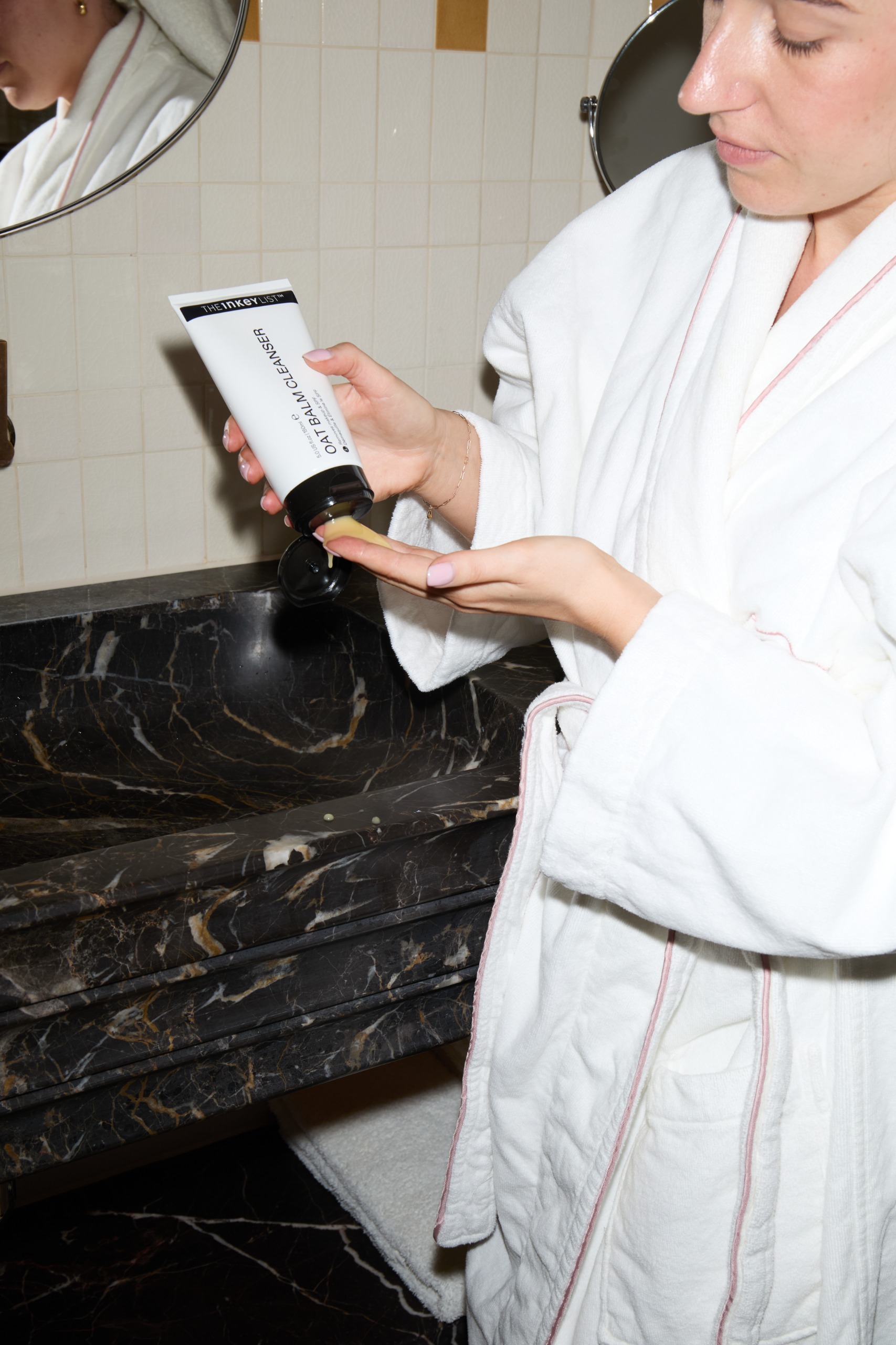 Grace Lindsay applying The Inkey List Oat Balm Cleanser next to a marble sink