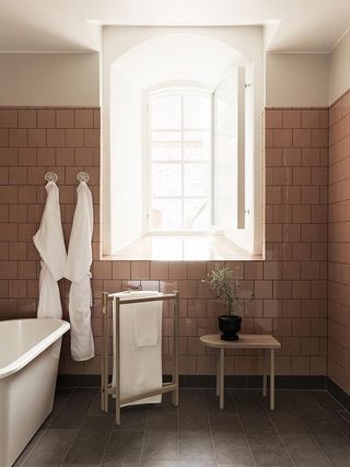 Bathroom with white bathtub, bay window, pink wall tiles and bathrobes hanging on wall