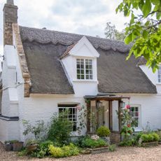 Exterior of pretty whitewashed cottage with thatched roof and roses by front porch