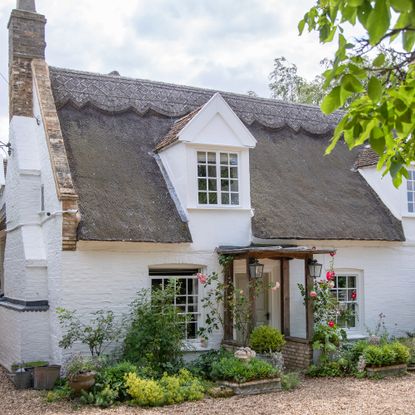 Exterior of pretty whitewashed cottage with thatched roof and roses by front porch