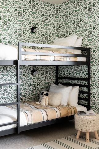 Green botanical print wallpaper in children's bedroom with wooden black painted bunks and cute stuffed animals
