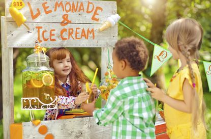 Little girl selling lemonade from a lemonade stand outdoors in summer to children